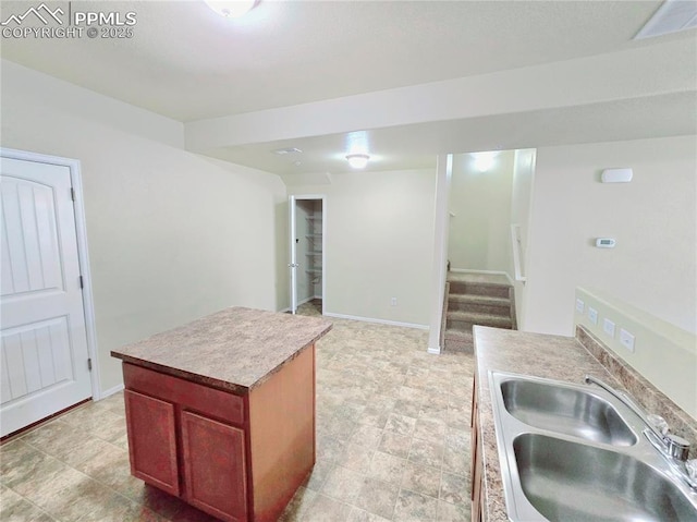 kitchen featuring a kitchen island, light countertops, baseboards, and a sink