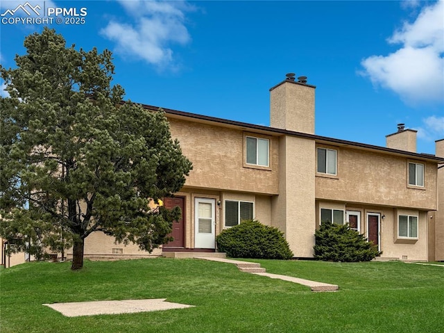 rear view of house featuring a yard, a chimney, and stucco siding