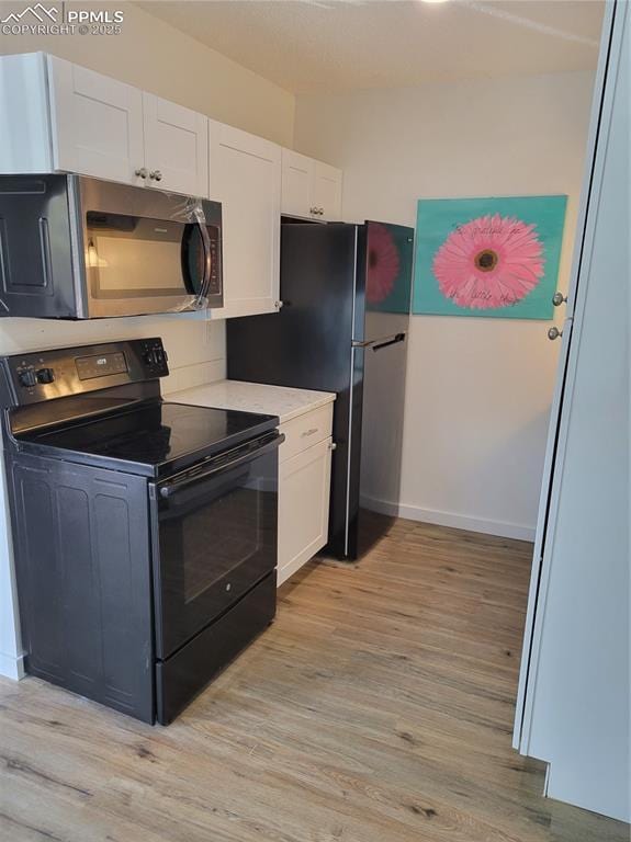 kitchen with light wood-style floors, light countertops, white cabinetry, and black appliances