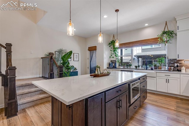 kitchen with stainless steel microwave, white cabinets, light wood finished floors, and pendant lighting