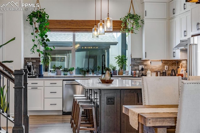 kitchen with white cabinetry, light wood-style flooring, decorative backsplash, under cabinet range hood, and dishwasher