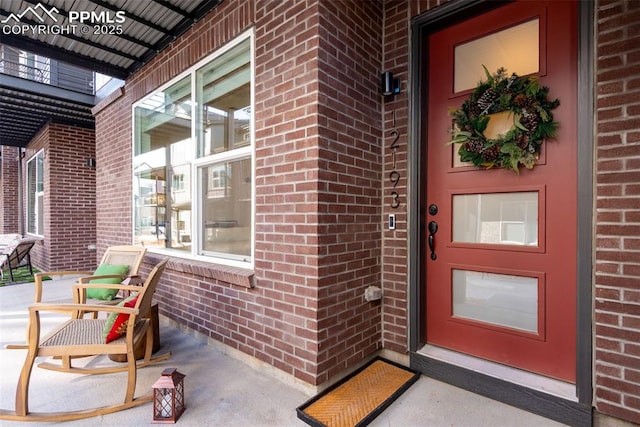 view of exterior entry featuring brick siding and a porch