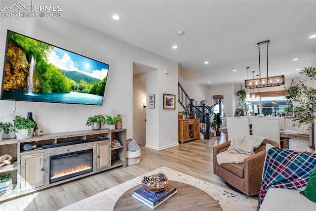 living room featuring baseboards, recessed lighting, stairs, light wood-style floors, and a glass covered fireplace