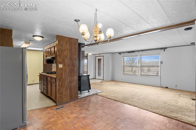 kitchen featuring visible vents, open floor plan, hanging light fixtures, freestanding refrigerator, and a wood stove