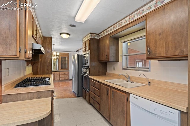 kitchen with under cabinet range hood, stainless steel appliances, a sink, light countertops, and tasteful backsplash