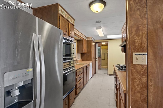 kitchen featuring brown cabinets, stainless steel appliances, light countertops, a sink, and under cabinet range hood