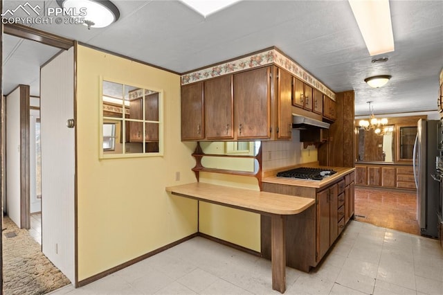 kitchen with light countertops, stainless steel gas stovetop, backsplash, a chandelier, and under cabinet range hood