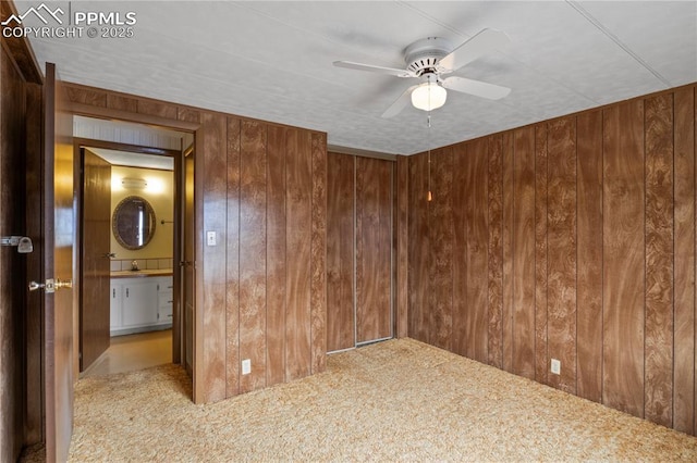 carpeted empty room with wood walls, a sink, and ceiling fan