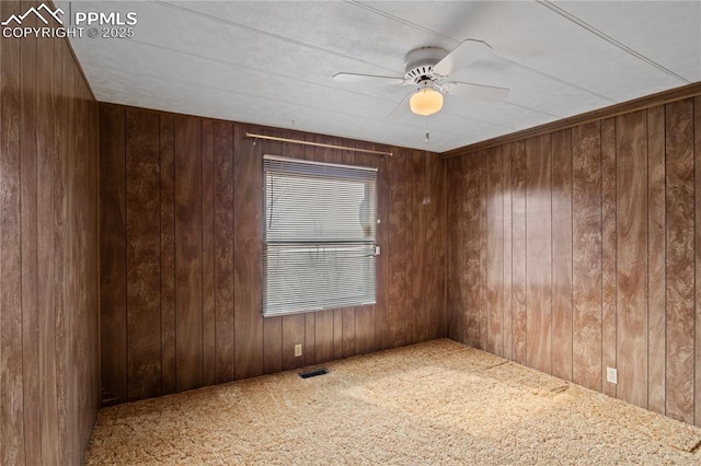 empty room featuring wooden walls, visible vents, and carpet flooring