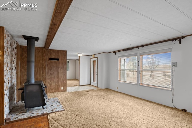 unfurnished living room with wood walls, beamed ceiling, and a wood stove