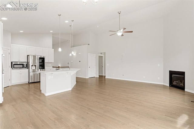 kitchen featuring a center island with sink, white cabinets, a glass covered fireplace, open floor plan, and stainless steel appliances