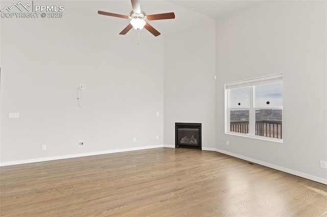 unfurnished living room with baseboards, wood finished floors, and a glass covered fireplace