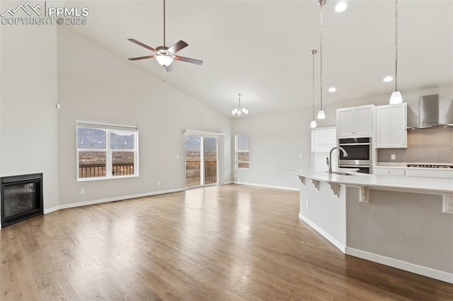 kitchen featuring a glass covered fireplace, open floor plan, wood finished floors, light countertops, and wall chimney range hood