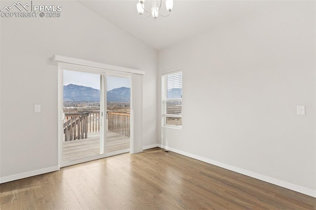 empty room featuring a chandelier, a mountain view, wood finished floors, baseboards, and vaulted ceiling