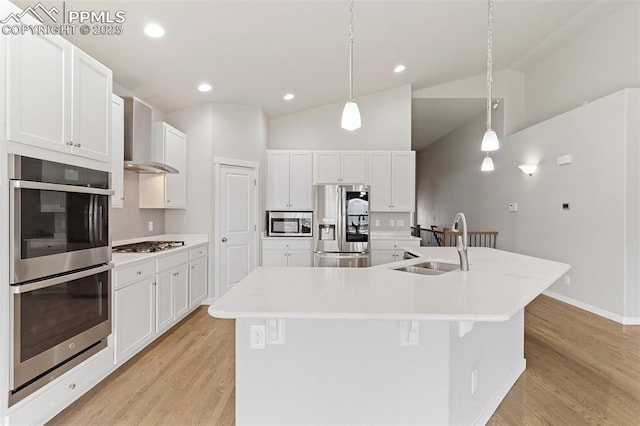 kitchen featuring stainless steel appliances, a spacious island, light wood-style floors, a sink, and wall chimney range hood