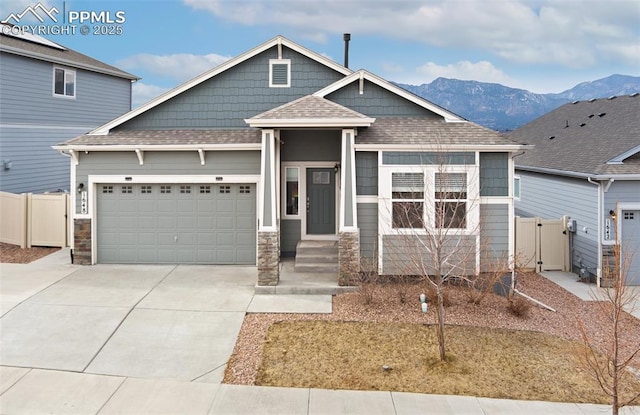 craftsman inspired home featuring a shingled roof, concrete driveway, an attached garage, fence, and a mountain view