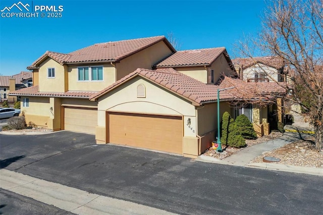 mediterranean / spanish house with a garage, a tile roof, driveway, and stucco siding