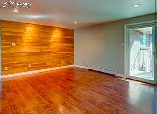 empty room with a baseboard heating unit, wood finished floors, and wood walls