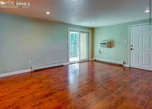 spare room with a baseboard radiator, baseboards, wood finished floors, and a wall unit AC