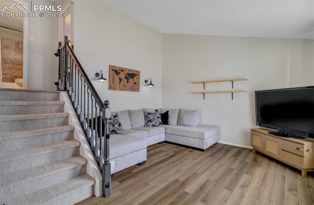 living room with stairway, baseboards, light wood-style flooring, and a textured ceiling