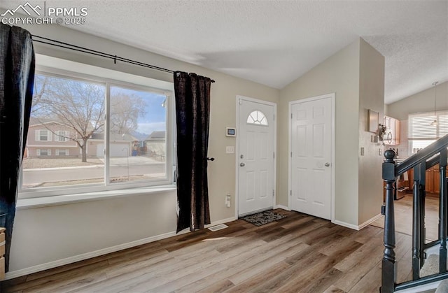 entryway with lofted ceiling, a textured ceiling, stairs, and wood finished floors