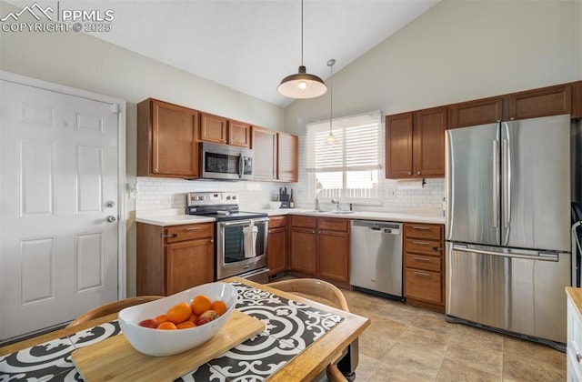 kitchen with stainless steel appliances, light countertops, hanging light fixtures, vaulted ceiling, and a sink