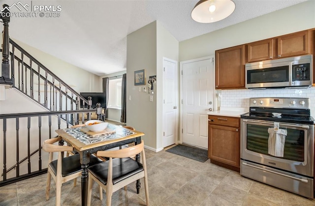 kitchen with baseboards, brown cabinetry, stainless steel appliances, light countertops, and backsplash