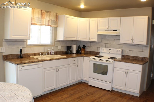 kitchen with under cabinet range hood, white appliances, dark countertops, and a sink