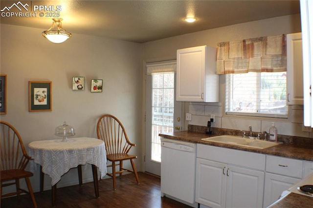 kitchen with white dishwasher, dark wood-style flooring, a sink, white cabinetry, and dark countertops