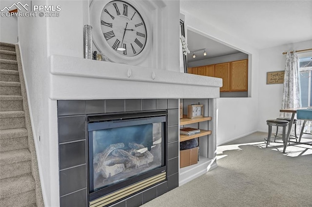 interior details featuring carpet floors, a tiled fireplace, rail lighting, and baseboards