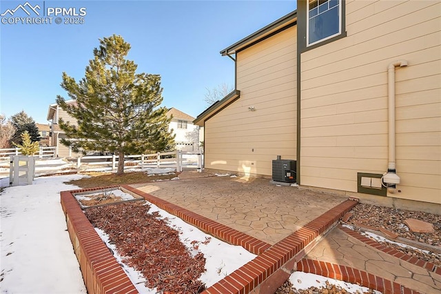 view of snow covered exterior with a vegetable garden, a patio area, fence, and central AC unit