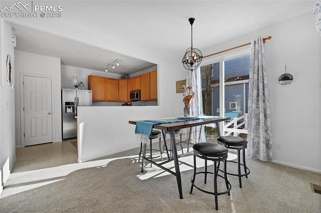 dining room featuring rail lighting, light carpet, baseboards, and an inviting chandelier