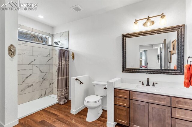 full bathroom with visible vents, toilet, a tile shower, vanity, and wood finished floors