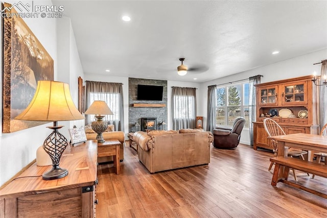 living area with a stone fireplace, wood finished floors, a ceiling fan, and recessed lighting