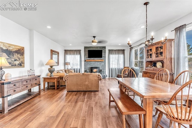 dining area with light wood-style floors, recessed lighting, ceiling fan with notable chandelier, and a stone fireplace