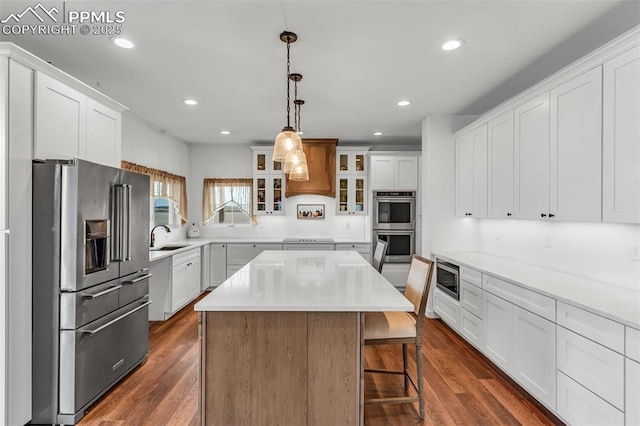 kitchen with a center island, appliances with stainless steel finishes, dark wood-type flooring, glass insert cabinets, and white cabinetry