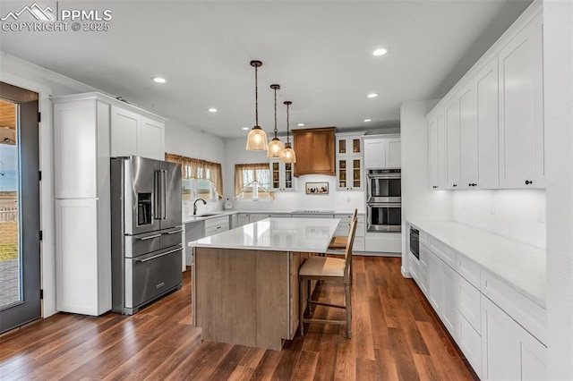 kitchen featuring dark wood-style flooring, a sink, appliances with stainless steel finishes, a center island, and glass insert cabinets