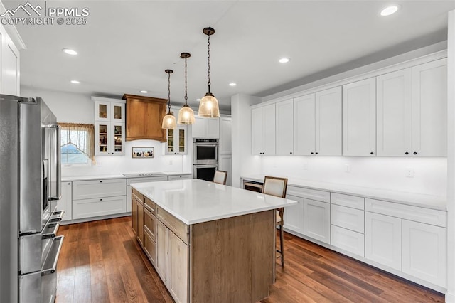 kitchen with appliances with stainless steel finishes, a center island, glass insert cabinets, and dark wood finished floors