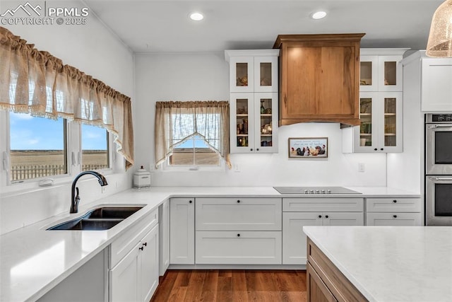 kitchen featuring dark wood-style flooring, black electric cooktop, stainless steel double oven, light countertops, and a sink