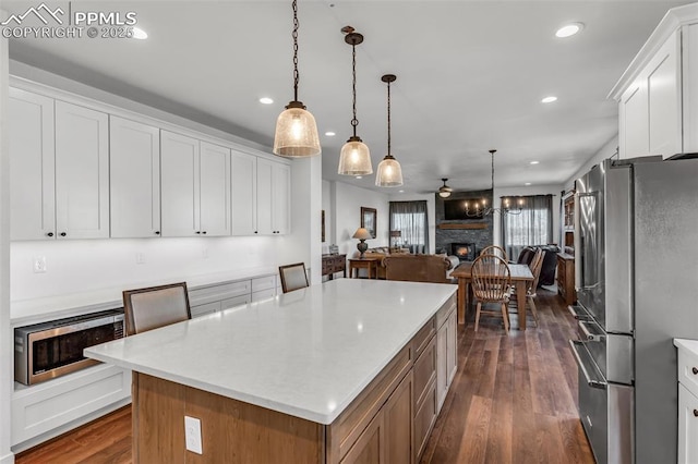 kitchen featuring a kitchen island, open floor plan, dark wood-type flooring, stainless steel appliances, and a stone fireplace