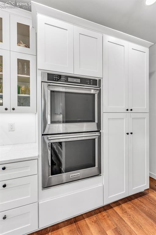 interior space with double oven, light wood-type flooring, white cabinetry, and glass insert cabinets