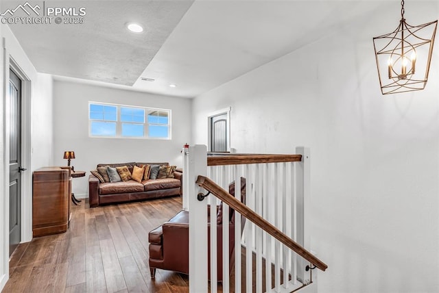 hall featuring visible vents, hardwood / wood-style flooring, an upstairs landing, and a notable chandelier