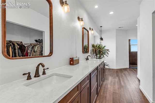 full bathroom with double vanity, a spacious closet, a sink, and wood finished floors