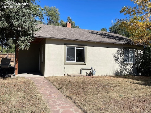 view of home's exterior featuring fence, roof with shingles, a lawn, stucco siding, and a chimney