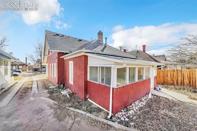 909 E 10th St, Pueblo, CO 81001 - view of home's exterior featuring a shingled roof, brick siding, fence, and a chimney
