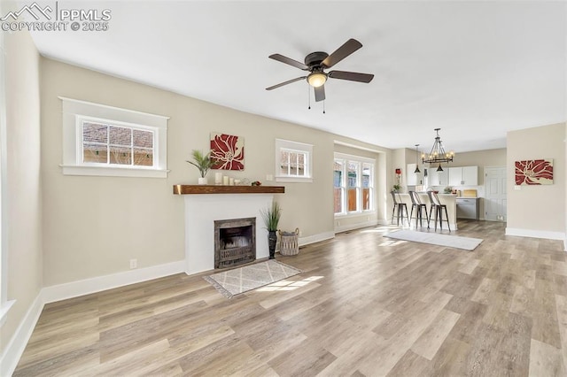 909 E 10th St, Pueblo, CO 81001 - unfurnished living room featuring light wood finished floors, baseboards, a tiled fireplace, and ceiling fan with notable chandelier
