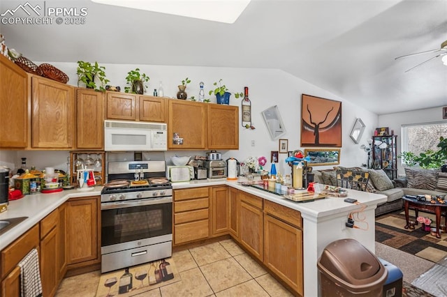 kitchen with a ceiling fan, a peninsula, light countertops, white microwave, and stainless steel gas range