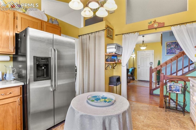 kitchen with hanging light fixtures, light countertops, stainless steel refrigerator with ice dispenser, and brown cabinets