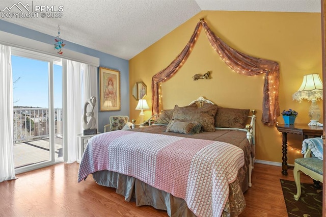 bedroom with lofted ceiling, a textured ceiling, wood finished floors, baseboards, and access to exterior