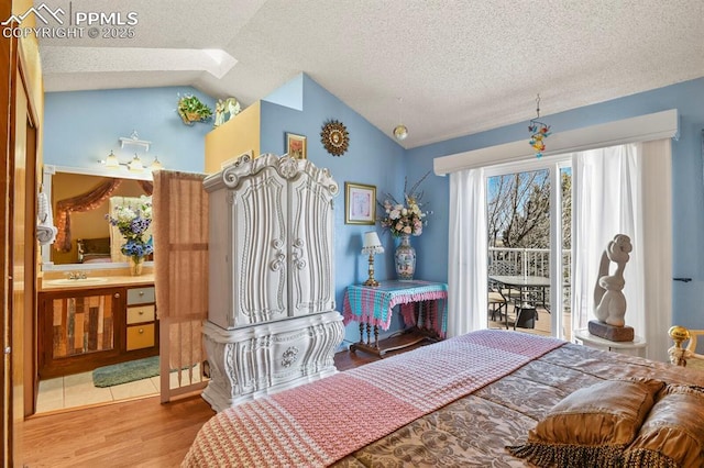 bedroom featuring access to exterior, lofted ceiling, wood finished floors, a textured ceiling, and a sink